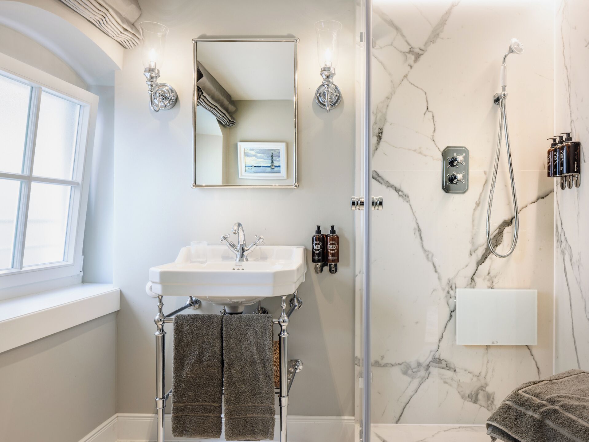A bathroom with a white sink, a mirror, a shower, and marble walls.