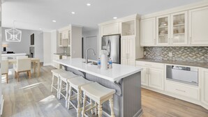 A modern kitchen with white cabinetry, a central island with bar stools, stainless steel appliances, and a tiled backsplash.