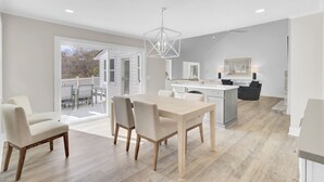A spacious living area with a dining table, chairs, a kitchen island, and a large window overlooking a deck.