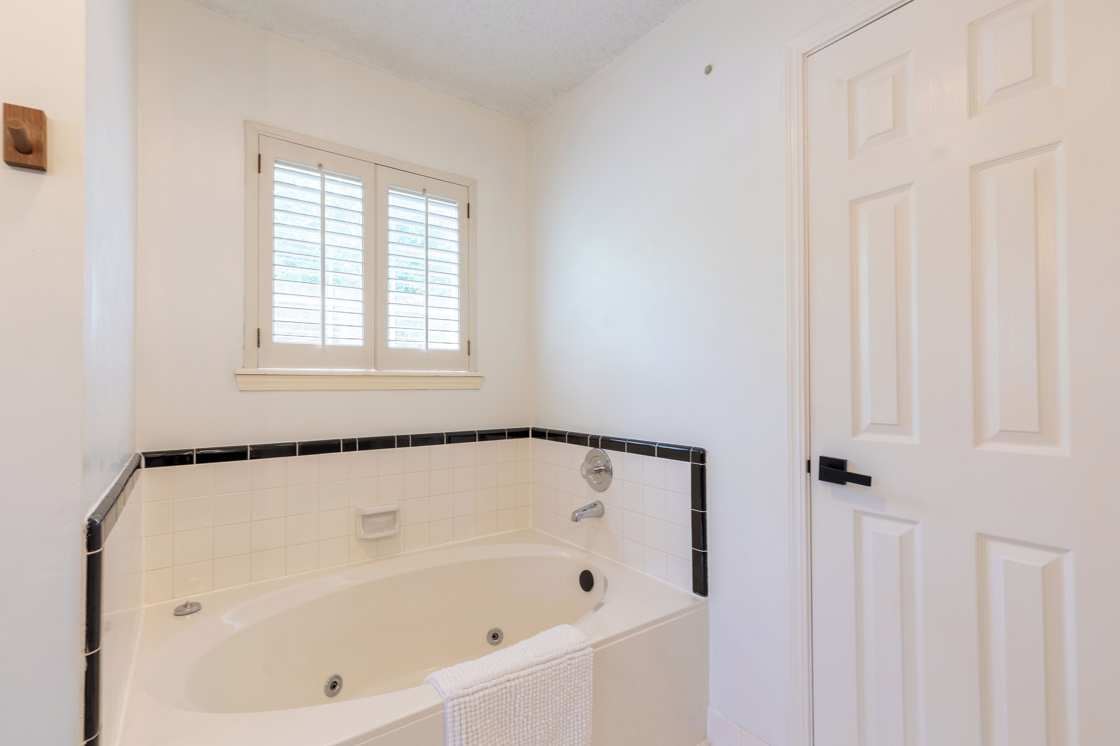 A bathroom with a bathtub, a window with blinds, and a white door.