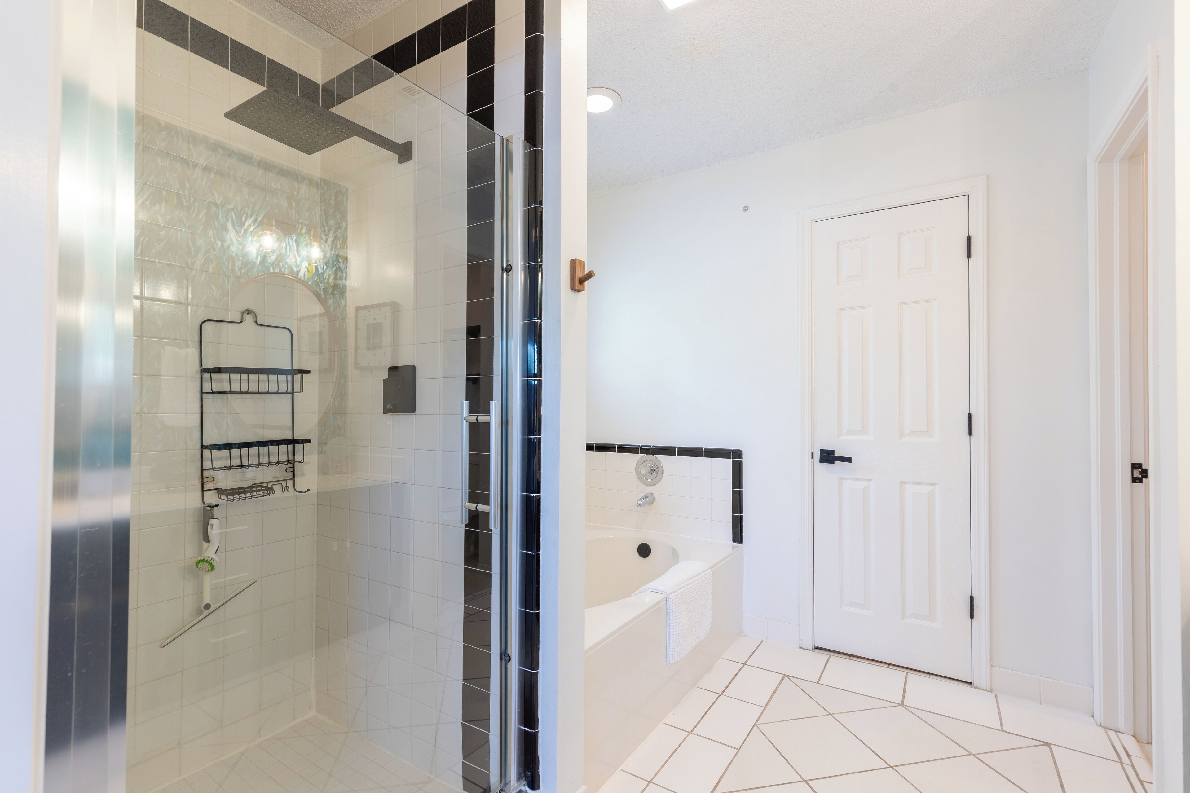 A bathroom with a glass shower enclosure, a bathtub, and a white door.