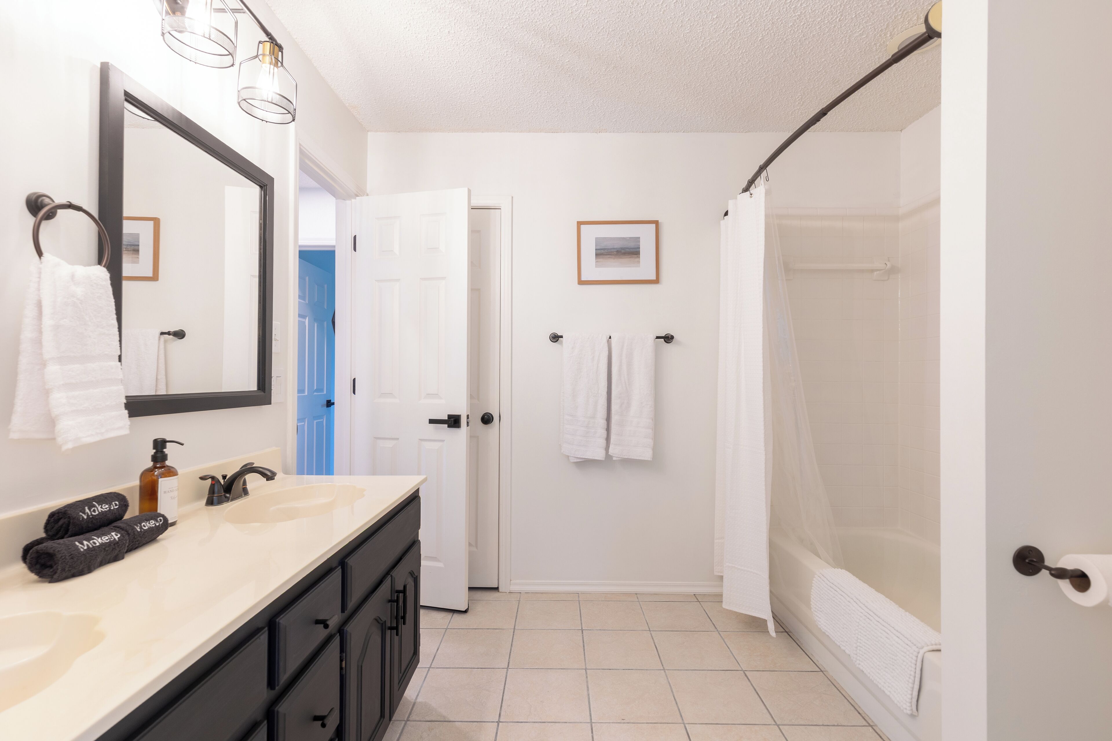 A bathroom with a white sink, black cabinets, a large mirror, and a shower with a curtain.