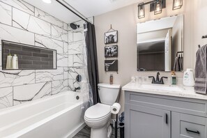 Une salle de bain moderne avec un mur en marbre, une baignoire, des toilettes et un meuble-lavabo avec un miroir.