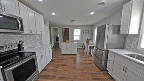 A modern kitchen with white cabinets, stainless steel appliances, and a wooden floor.