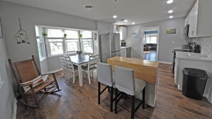 A modern kitchen with white cabinets, a wooden dining table, and a rocking chair.