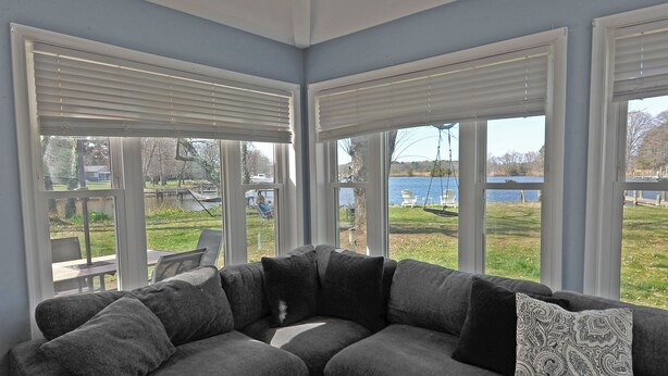 A corner living room with a sectional sofa, large windows, and a view of a lake and outdoor furniture.