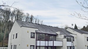 Ett modernt hus i två våningar med ett sluttande tak, stora fönster och en liten balkong.