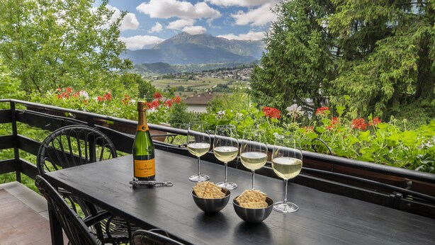 A table with a bottle of wine, glasses, and crackers on a balcony with a scenic view of mountains and greenery. - Garden Apartment Relax (Barco)