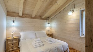 A wooden-paneled bedroom with a bed, two bedside tables, and a window. - Garden Apartment Relax (Barco)