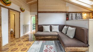 A cozy room with a wooden ceiling, a brown sofa with pillows, a patterned rug, and a stone wall with a light fixture. - Garden Apartment Relax (Barco)