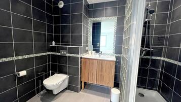 Une salle de bain moderne avec des carreaux noirs, un meuble-lavabo en bois, des toilettes blanches et une douche à parois de verre.