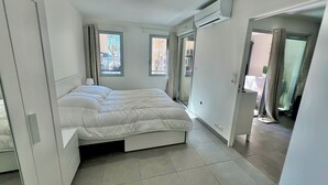 Ein modernes Schlafzimmer mit Bett, Fenster, Klimaanlage und einer Tür zu einem anderen Raum.