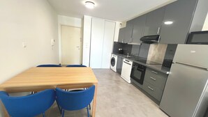 Eine kompakte Küche mit einem Holztisch und blauen Stühlen, einer Waschmaschine, einem Geschirrspüler und einem Kühlschrank.