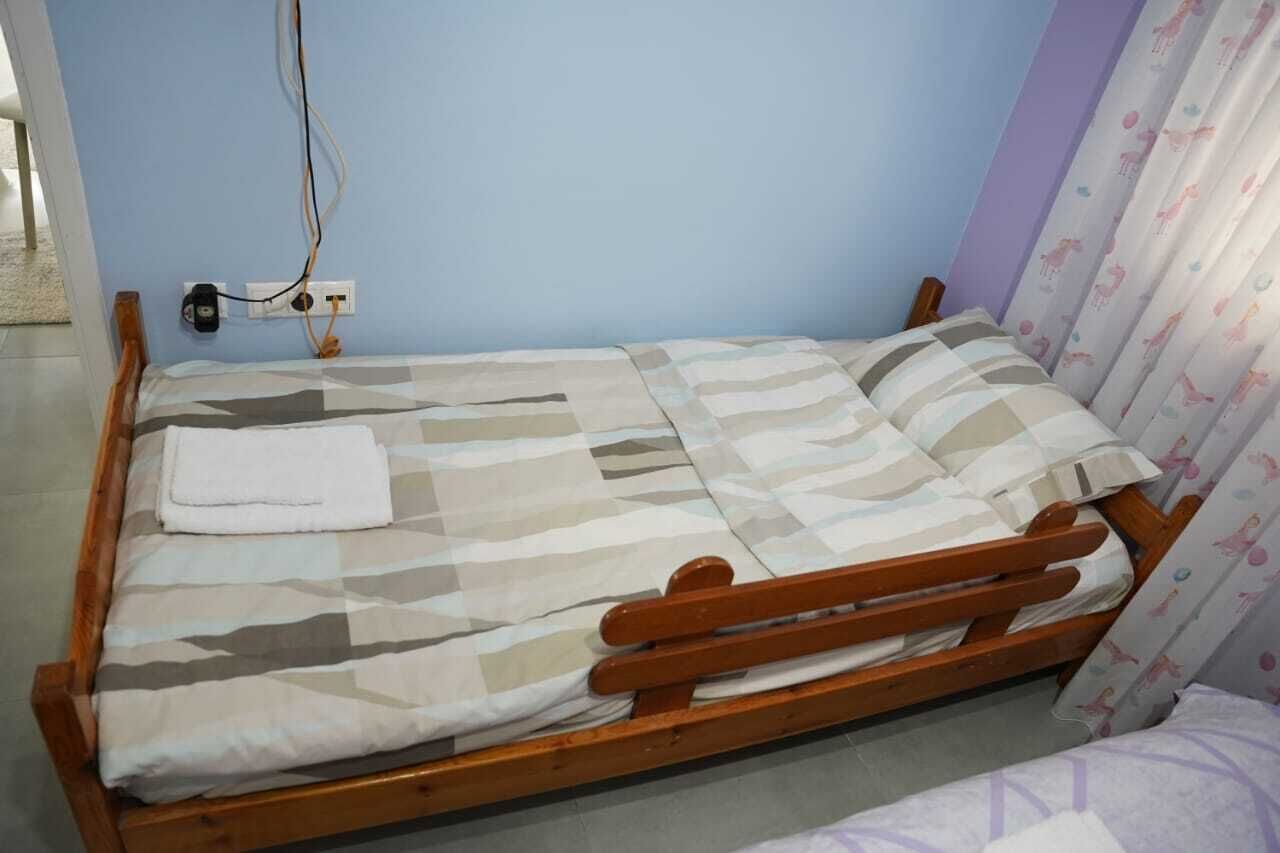 A single bed with a wooden frame, a striped bedspread, and a white towel on the bed.