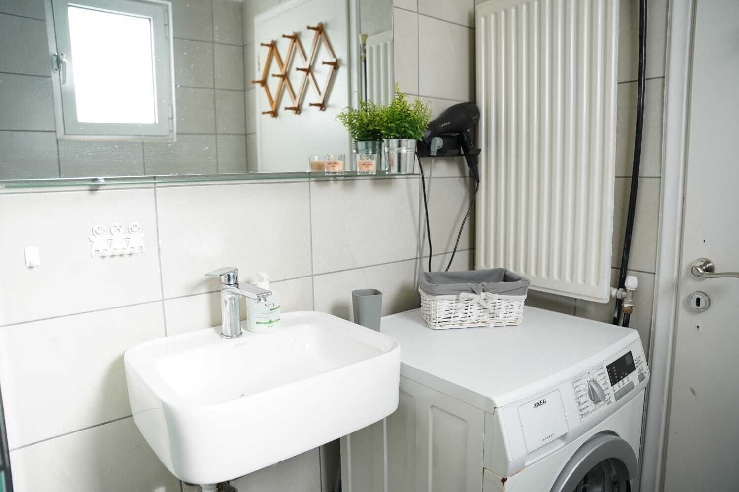 A modern bathroom with a white sink, a mirror, a hairdryer, and a washing machine.