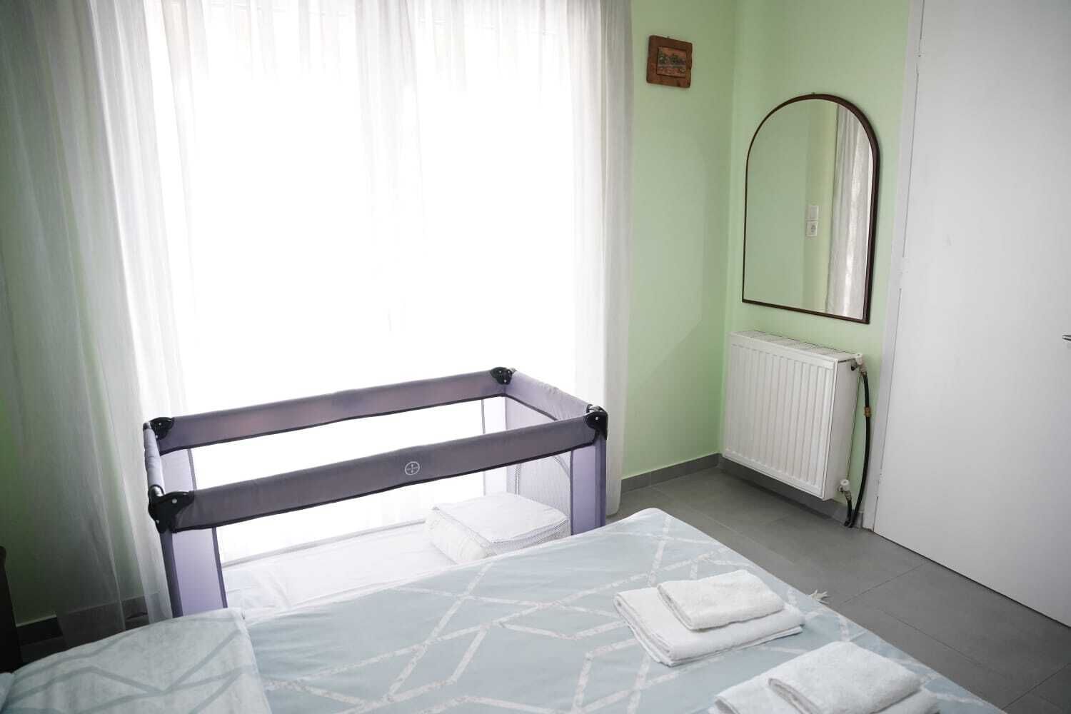 A simple, clean room with a bed, a window with curtains, a radiator, and a mirror on the wall.