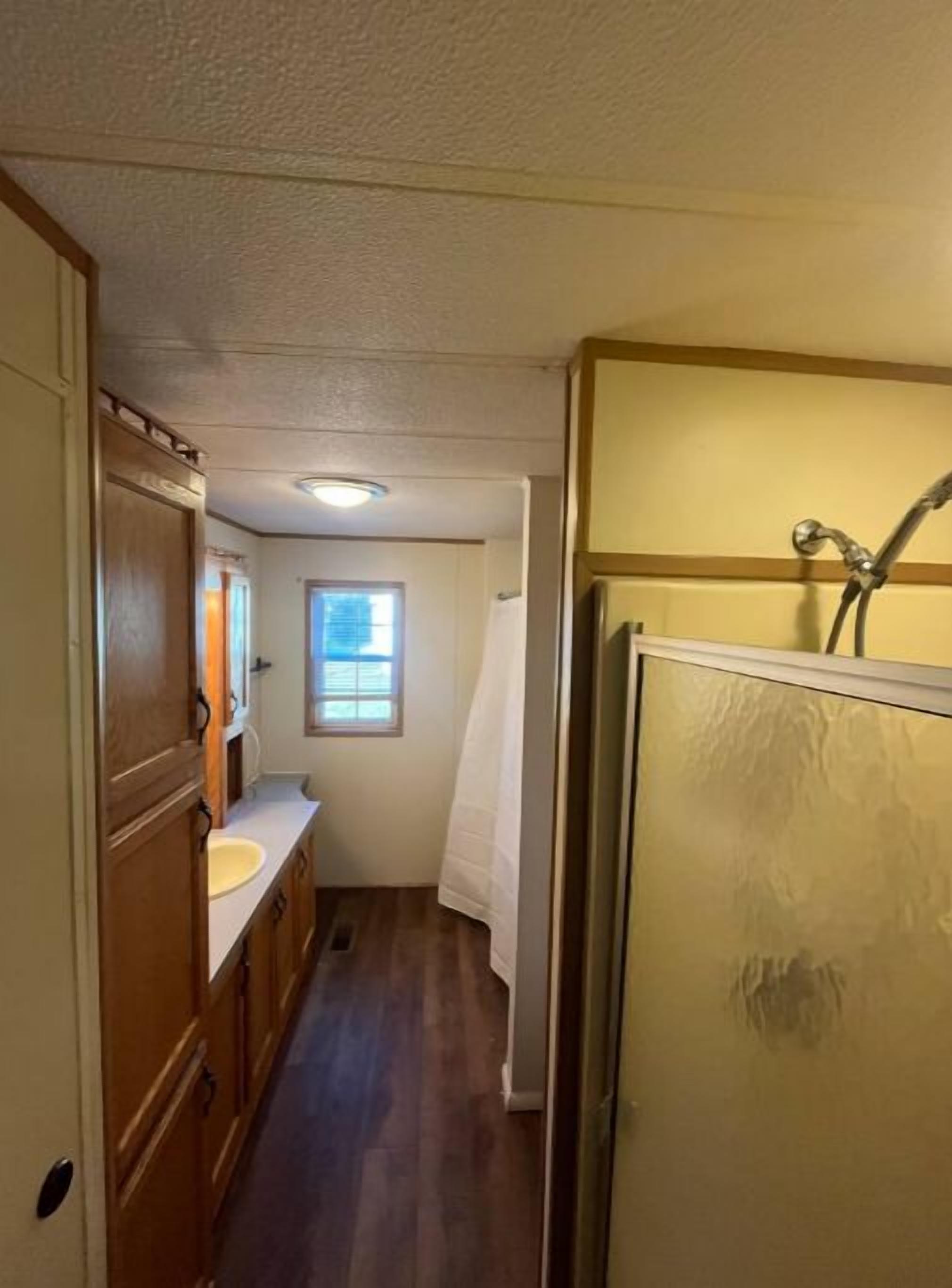 A narrow hallway with wooden cabinets, a sink, and a shower area.