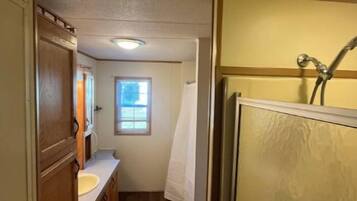 A narrow hallway with wooden cabinets, a sink, and a shower area.