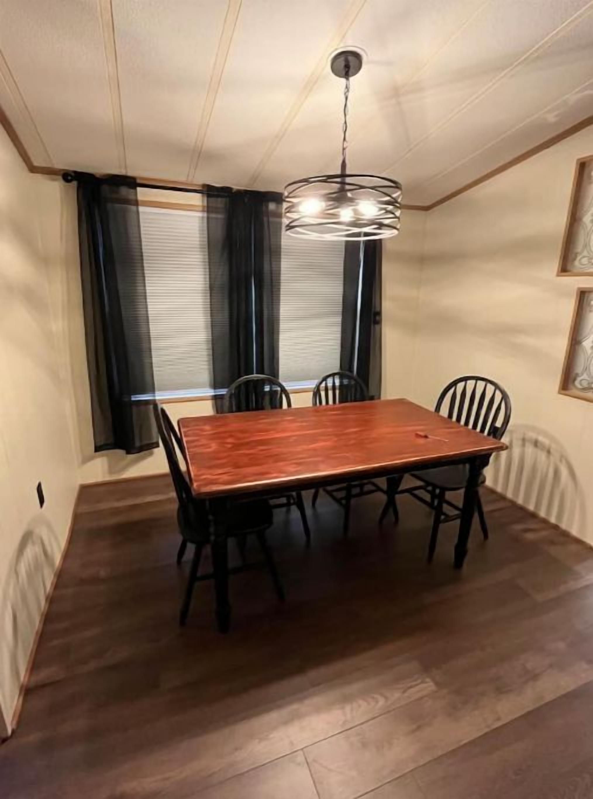 Zona pranzo con tavolo e sedie in legno, lampadario a sospensione e finestra con tende.