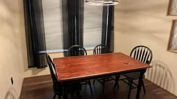 Zona pranzo con tavolo e sedie in legno, lampadario a sospensione e finestra con tende.
