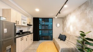 A modern kitchen with a stainless steel refrigerator, microwave, and stove. There is a yellow rug, a grey sofa, and a potted plant. - Tranvia 40 (Medellín)