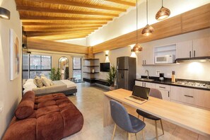 A modern kitchen with wooden beams, a dining area with a laptop, and a cozy seating area with a sofa and cushions.