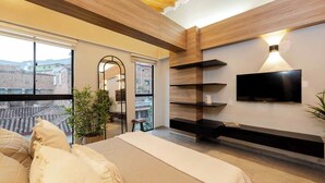 A modern bedroom with a large bed, a TV mounted on the wall, and a balcony with a view of buildings. - Tranvia 40 (Medellín)