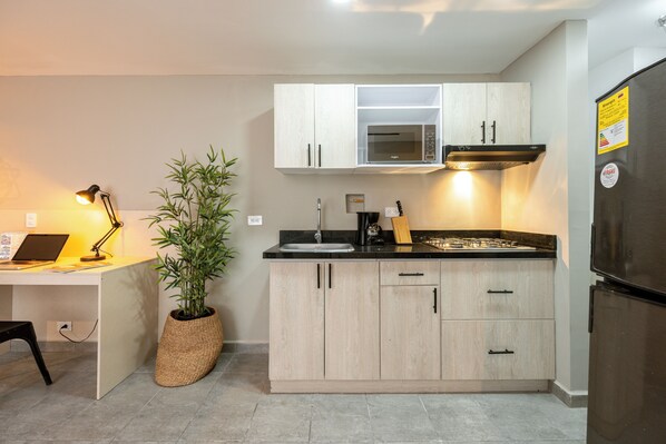 A modern kitchen with light wood cabinets, a built-in microwave, and a stainless steel refrigerator.