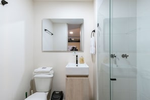A modern bathroom with a toilet, sink, and glass-enclosed shower. - Tranvia 40 (Medellín)