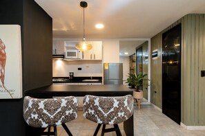 A modern kitchen with a central island, two patterned chairs, a hanging light fixture, and a potted plant. - Tranvia 40 (Medellín)