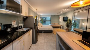 A modern kitchen with a built-in microwave, refrigerator, and coffee maker. There is a dining area with a laptop on the table and a sofa in the background. - Tranvia 40 (Medellín)