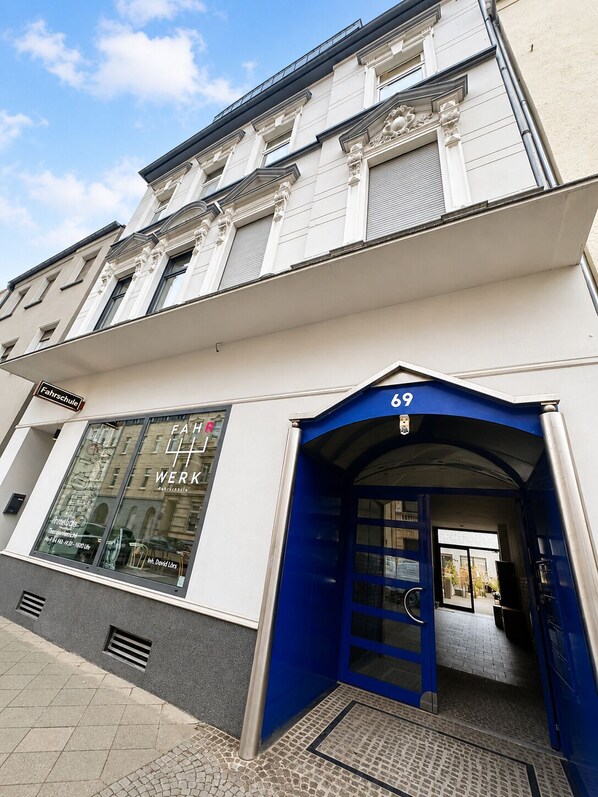 A building with a blue entrance, a visible shop window with bicycles, and a sign indicating a school.