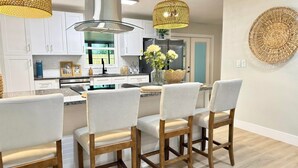 A modern kitchen with white cabinets, a central island with bar stools, and decorative woven light fixtures.