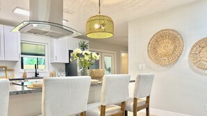 A modern kitchen with white cabinetry, a central island with bar stools, and a hanging woven light fixture.