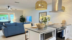 A modern kitchen with a built-in island, oven, and microwave. There is a blue sofa and a dining area with a table and chairs.