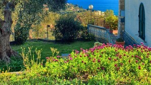 A coastal building with a red-tiled roof, surrounded by lush greenery and flowering plants. - Cottage with pool, A/C and wi fi (IMPERIA)