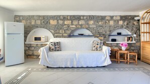 A cozy living room with a stone wall, a white sofa, a small table with a vase, and a white refrigerator. - Cottage with pool, A/C and wi fi (IMPERIA)