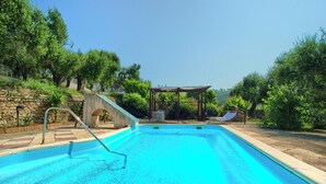 A swimming pool with a stone wall, a pergola, and a lounge chair. - Cottage with pool, A/C and wi fi (IMPERIA)