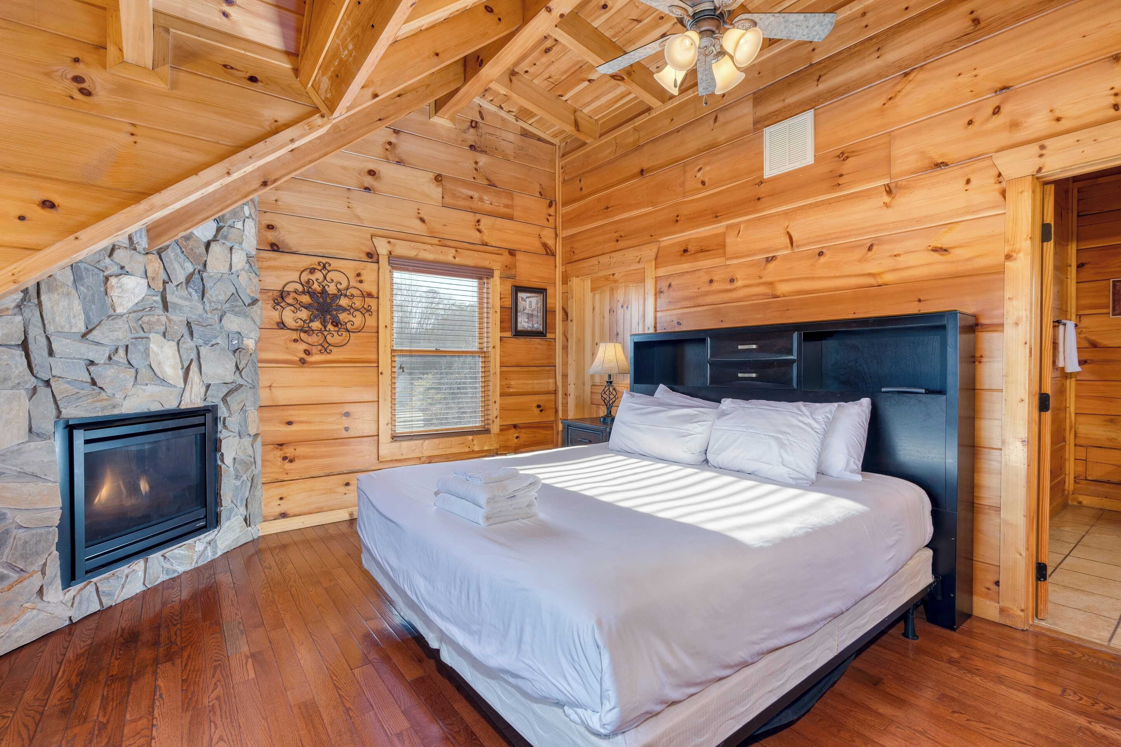 Ein Schlafzimmer in einer Blockhütte mit Kamin aus Stein, einem Bett mit weißer Bettwäsche und einem Deckenventilator.