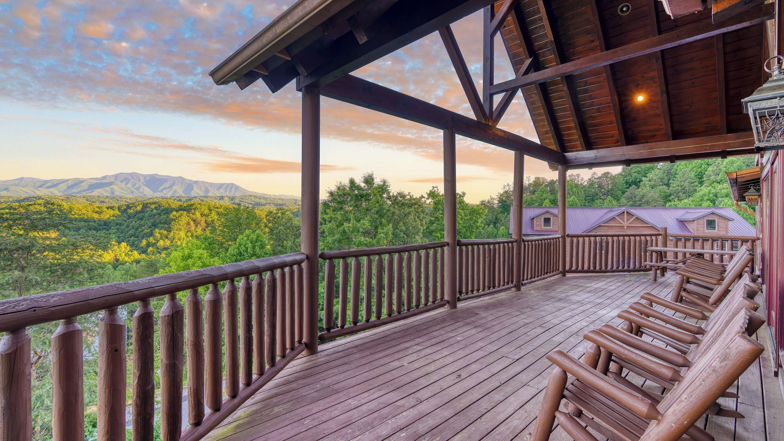 Eine Holzterrasse mit Geländer, mit Blick auf eine bewaldete Landschaft und Berge.
