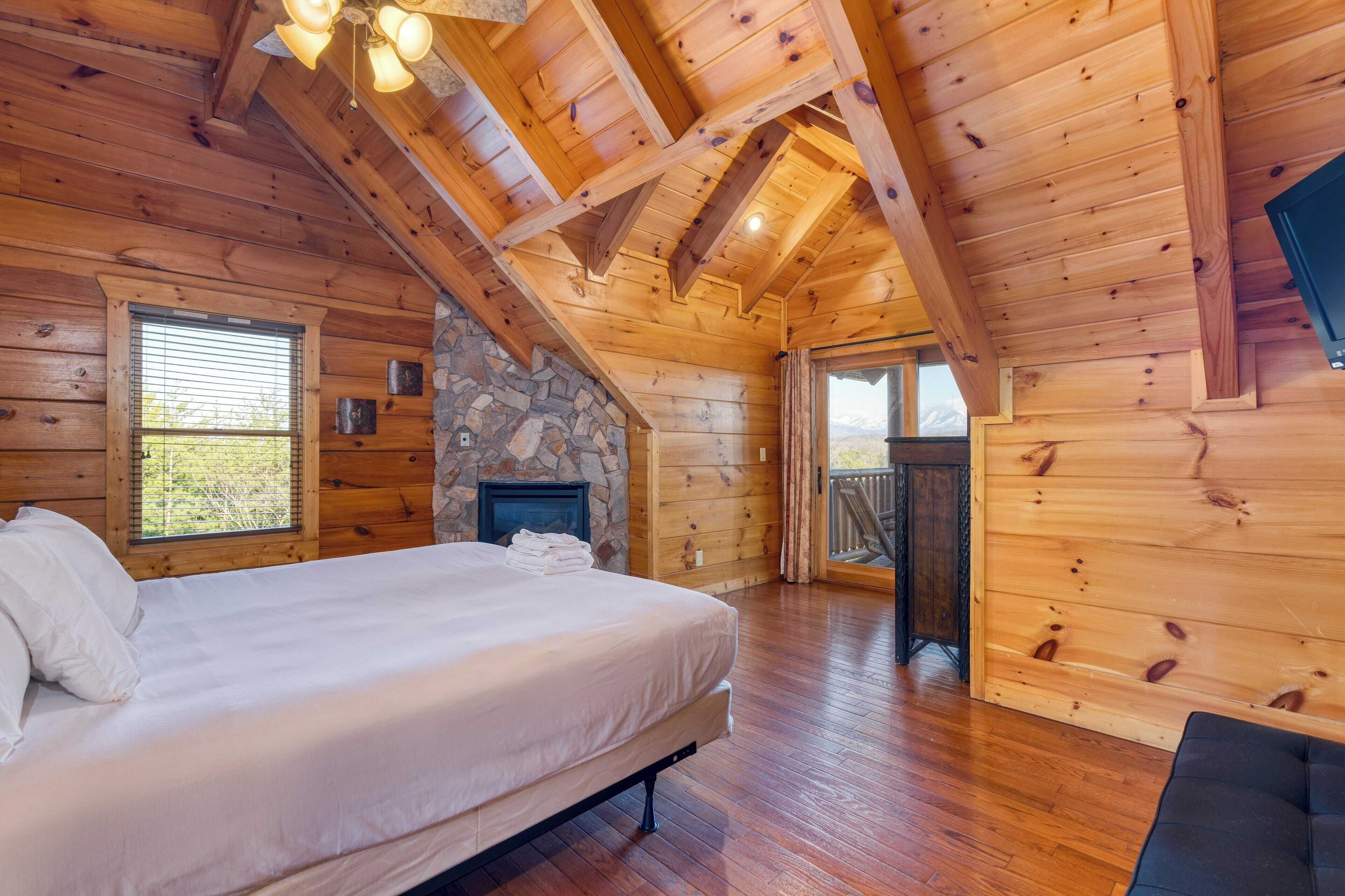 A wooden cabin bedroom with a bed, a stone fireplace, and a large window.
