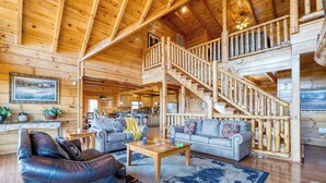 Spazioso interno di una baita di legno, con zona soggiorno, sala da pranzo e una scala che conduce a un piano superiore.