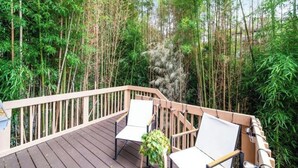 A wooden deck with two white chairs and a potted plant, surrounded by dense bamboo forest.