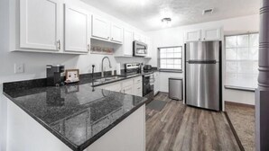 A modern kitchen with white cabinets, a stainless steel refrigerator, and a granite countertop.