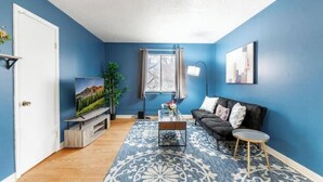 A living room with a blue wall, a black sofa, a coffee table, and a TV on a stand. - OSU - Heart of Short North -STEPS from High ST-OSU (Columbus)