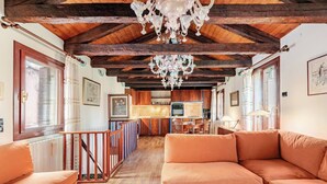 Un salón amplio con techo de madera, una araña y una cocina al fondo.