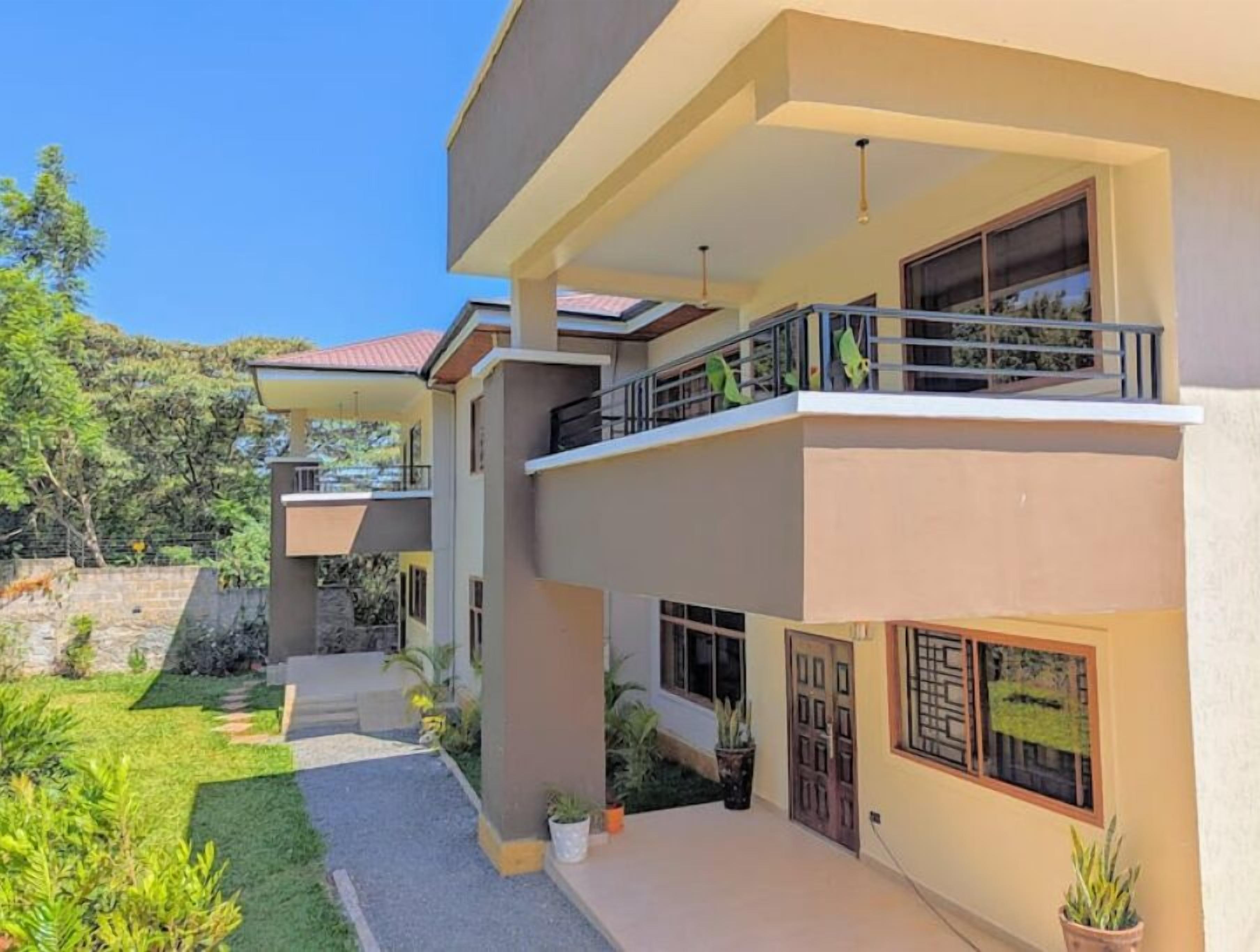 A modern two-story house with a balcony, a stone wall, and a well-maintained garden.
