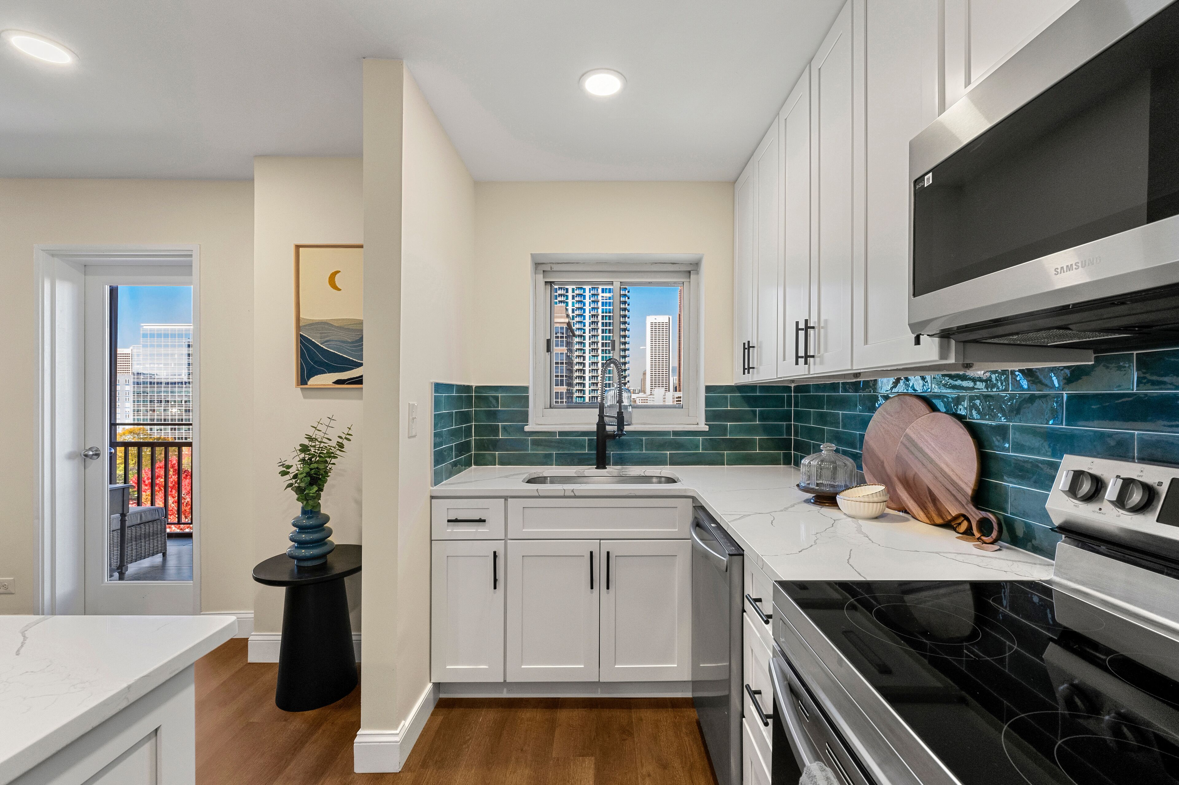 A modern kitchen with white cabinets, a black stove, and a view of tall buildings through a window.