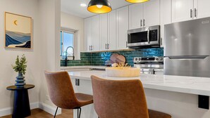 A modern kitchen with white cabinets, stainless steel appliances, and two brown chairs with black metal legs. - Stylish 1-bedroom condo Downtown Atlanta (Atlanta)
