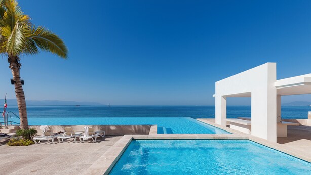 A swimming pool with a view of the ocean, lounge chairs, and a palm tree. - Entire condo in Puerto Vallarta, Mexico (Puerto Vallarta)